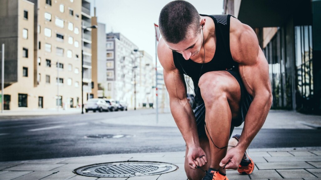 Gemotiveerde sporter strikt zijn veters voor een hardloopsessie in de stad, focus op motivatie door video’s.